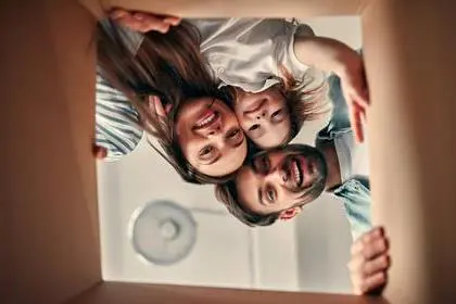 Family on moving day. Attractive young woman and handsome bearded man with their cute little daughter are happy to move into new home. Looking into cardboard box together.
