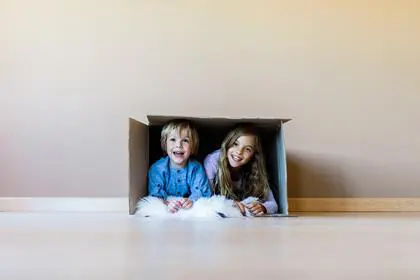 Happy brother and sister having fun while being inside of carton box against the wall. Girl is looking at camera. Copy space.