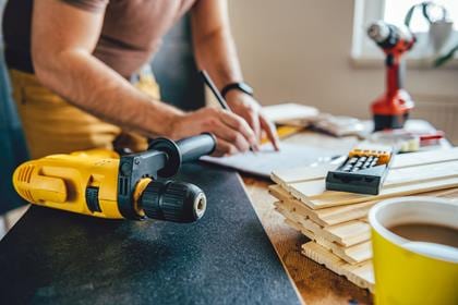 Yellow power drill and man making draft plan using pencil on the table with tools in the background