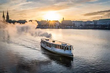 steamboat on Alster Lake in Hamburg, Germany with cityscape in background during sunset